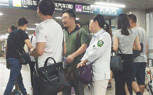 北京西站A1出口，一名女医托身着带有“北京公交集团”字样的衣服，与两名同伙聊天。（据新京报）